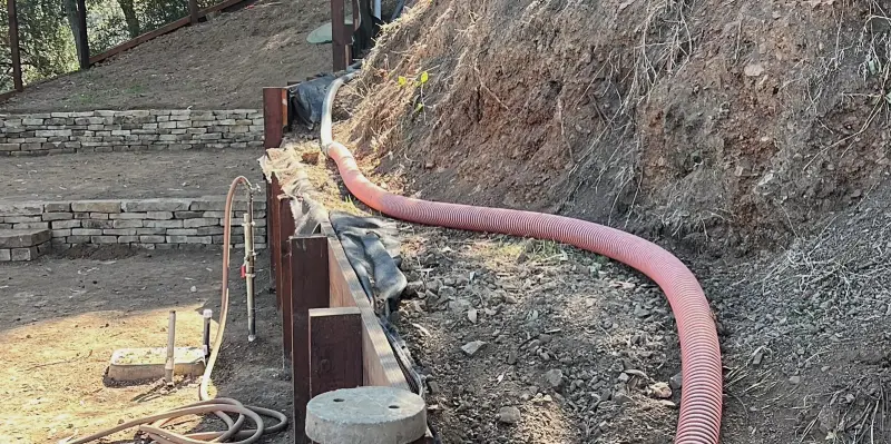 A pumping hose run down a steep hillside lot to reach a septic tank
