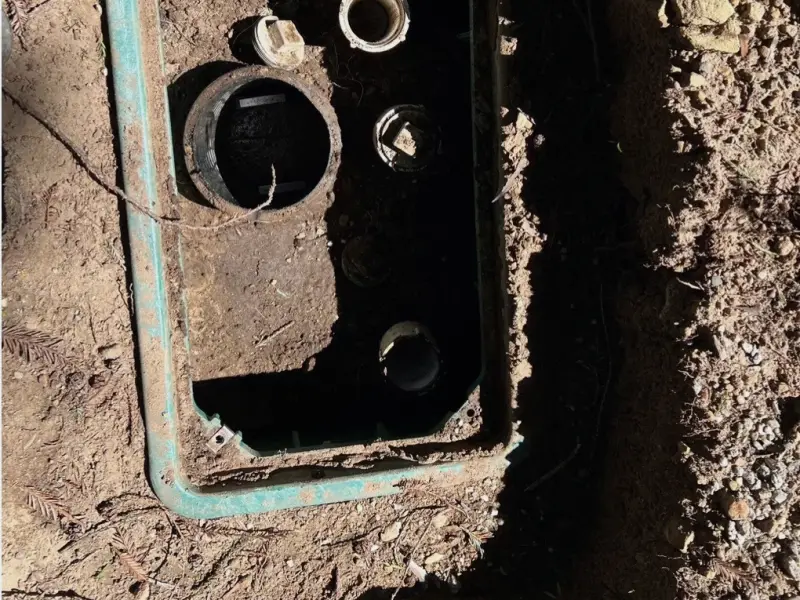 An opened septic riser box showing the tank inlet and outlet