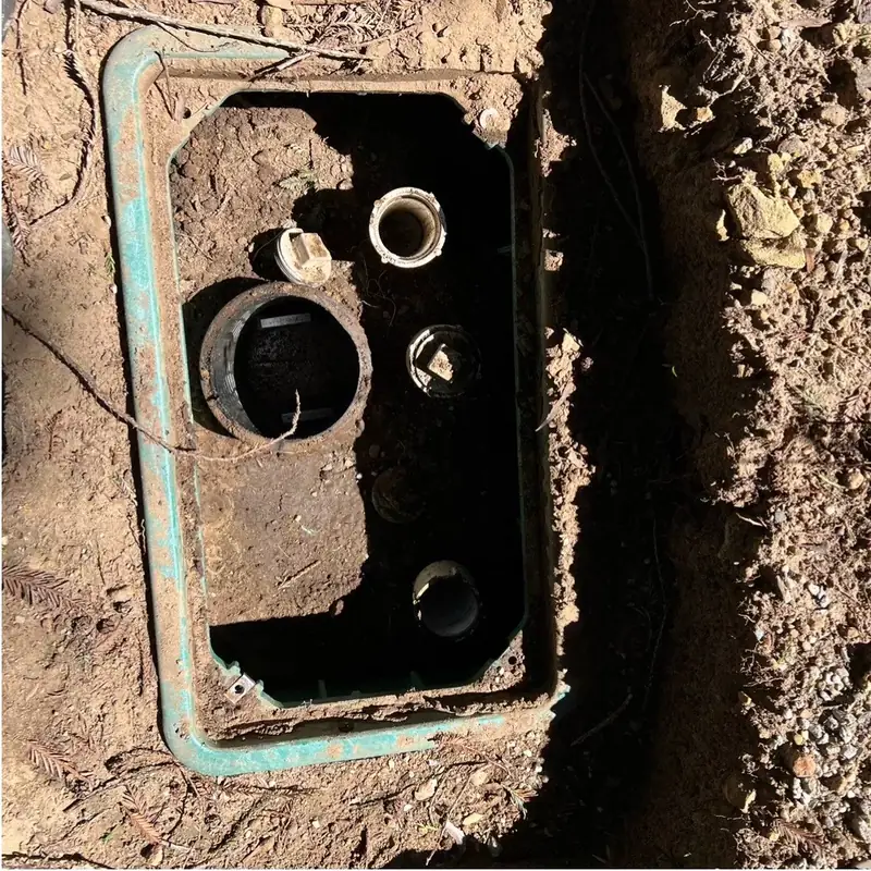 An uncovered distribution box with inlet and outlet pipes, dug out for inspection