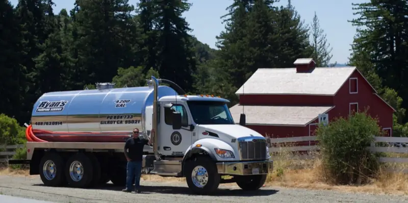 Ryan's vacuum truck parked in front of a red barn, with Ryan beside the cab